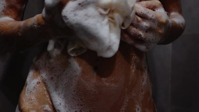 Slender woman applying soapy foam with washcloth on her stomach in shower