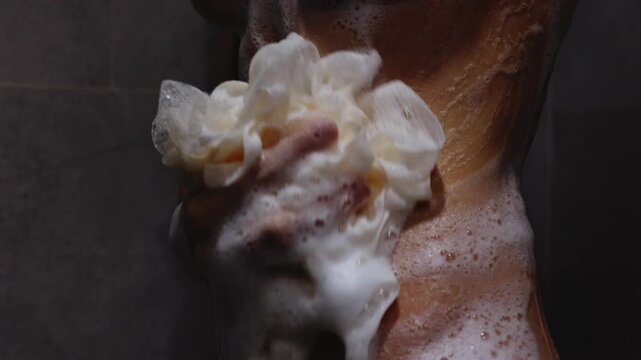 Slender woman applying soapy foam with washcloth on her stomach in shower. Side view