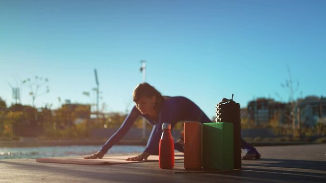 young beautiful woman practicing yoga at sunset outdoors, body conscious person exercising stretching with foam roller, blocks, scented indian sticks and other accessories, balance and harmony concept