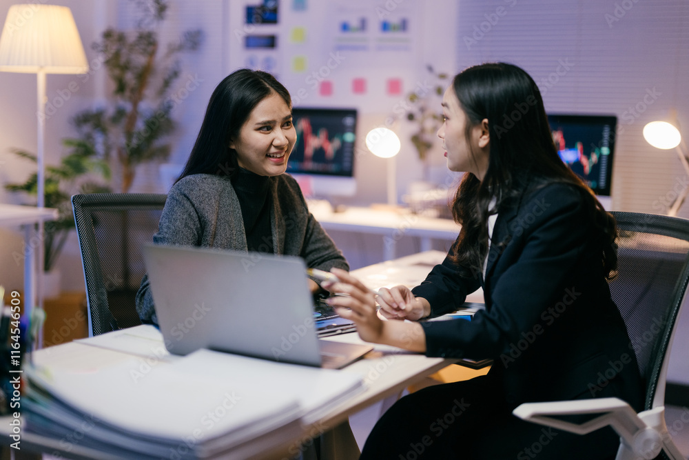 Poster two young businesswomen are working together on a project in a modern office at night, discussing st
