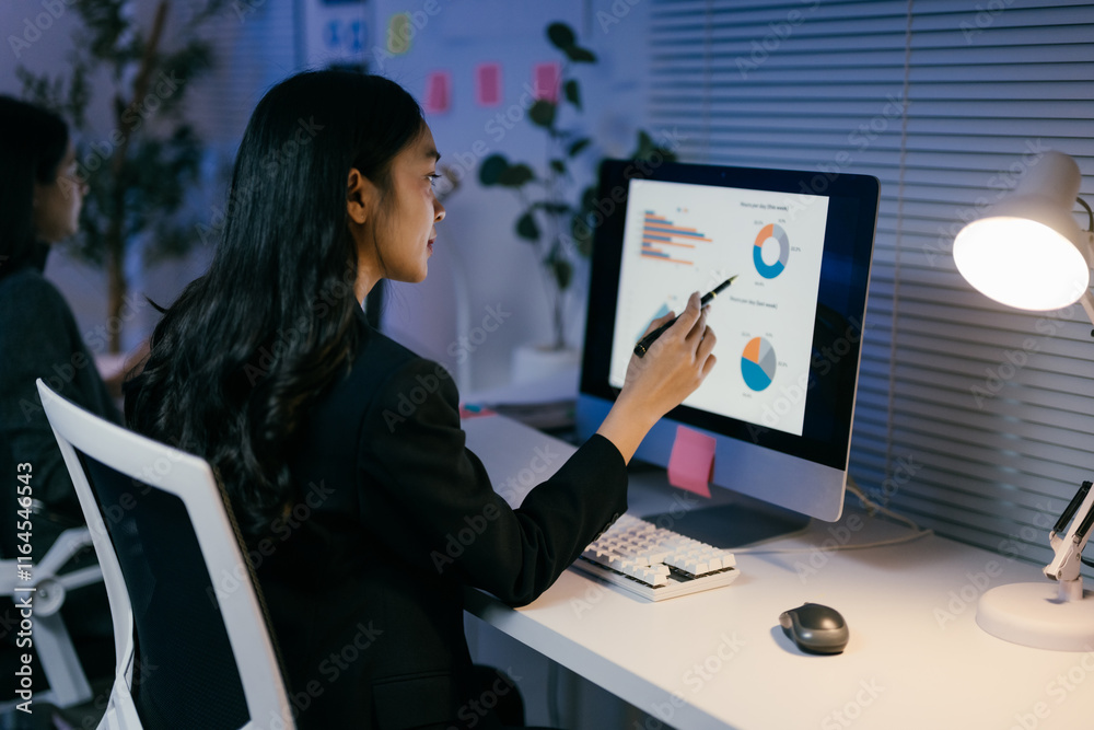 Poster businesswoman is pointing at charts on a computer screen with a pen, working late in the office, ill