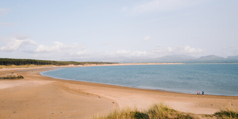Panoramic view of Newborough beach with people walking along the coast