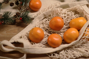 Festive details. Juicy tangerines in net mesh bag on wooden table, pine garland. Top view. 
