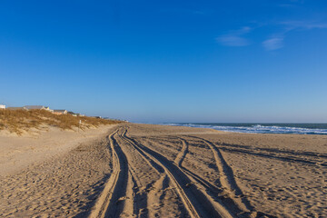 a beautiful sunrise at the beach with footprints in the sand and tall grass, ocean water and waves, blue sky and clouds in Carolina Beach North Carolina USA