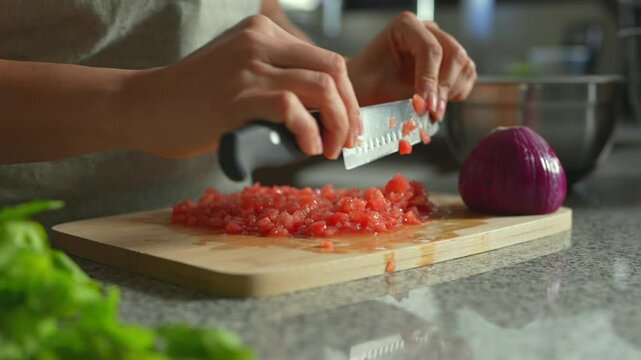 Mujer picando tomate en tabla de madera en la cocina con cuchillo a dos manos para preparar guacamole