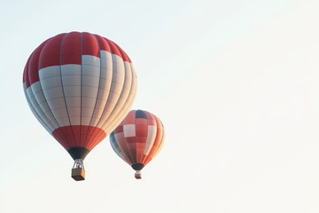 Fototapeta premium Two hot air balloons are flying in the sky. One is red and white and the other is orange and white