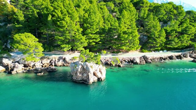 A stunning aerial view of Brela, Croatia, showcasing the iconic Kamen Brela rock formation surrounded by crystal-clear turquoise waters. The coastline is dotted with pristine beaches