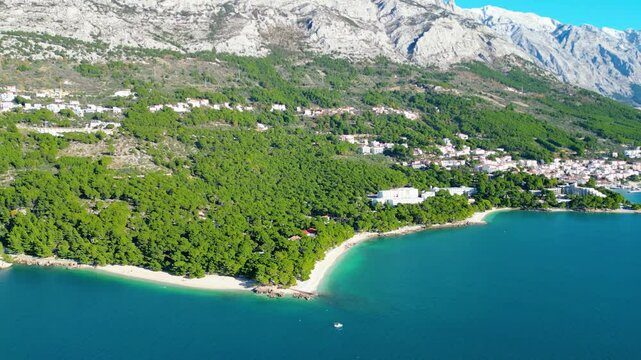 A stunning aerial view of Brela, Croatia, showcasing the iconic Kamen Brela rock formation surrounded by crystal-clear turquoise waters. The coastline is dotted with pristine beaches