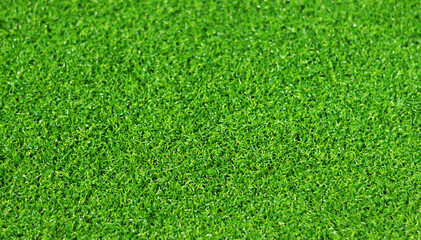 Artificial green grass mat, selective focus. Artificial turf, surface made of synthetic fibers. Green grass texture background. Short artificial grass golf surface