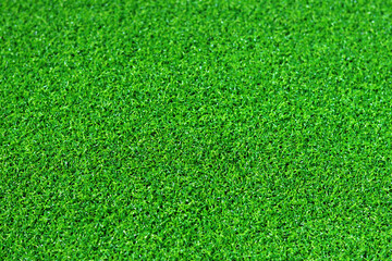 Artificial green grass mat, selective focus. Artificial turf, surface made of synthetic fibers. Green grass texture background. Short artificial grass golf surface