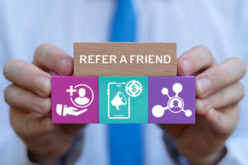 Person holding colorful blocks with icons sees inscription: REFER A FRIEND. People making money from referral. Refer a friend or referral marketing business concept. Social media marketing for friends