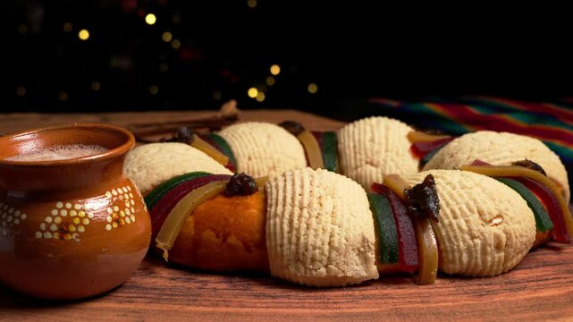 Traditional rosca de reyes and Mexican hot chocolate on a wooden table, blurred lights in the background