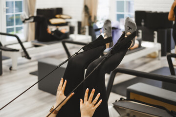 Person doing leg-up while practicing pilates on reformers in studio. Legs close-up in gym, 