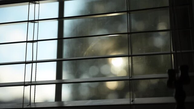 Looking at sunset through window closed by blinds and sun rays