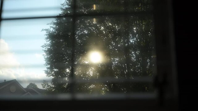 Looking at sunset through window closed by blinds and sun rays. Close up