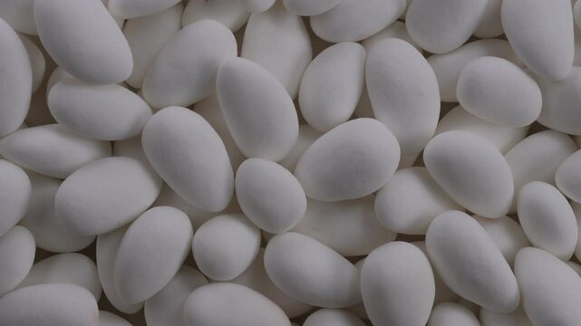 Top down view. Heap of white chocolate covered almond nuts. Glazed white dragees. Slider shot. Candies, sweet treats, snacks, confectionery concepts. 4k