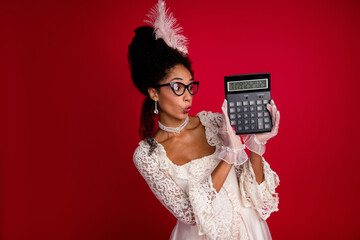 Young woman in elegant lace gown holds oversized calculator against a vivid red backdrop, merging...