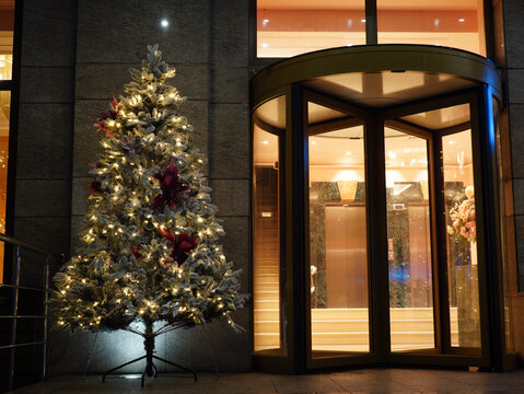 Pretty Christmas tree decorated with snowy powder and red flowers near rotating entrance door of modern restaurant in center of Bucharest