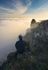 Autumn morning. Traveler on the top of rock above river valley with thick fog. Nature of Ukraine