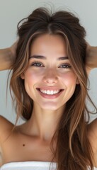 Naklejka premium A beautiful young woman with long, flowing hair smiles brightly, her hands playfully tousling her locks. Her glowing skin and joyful expression radiate positivity and confidence, making this image