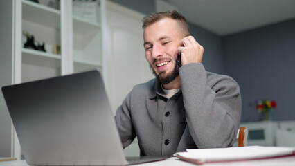 Businessman working from home talking on phone and using laptop smiling