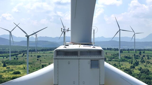 Close up view of a wind turbine nacelle with large blades, surrounded by multiple turbines in a green landscape, emphasizing renewable energy technology, sustainability, and innovation.