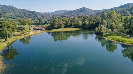 Serene lake nestled in a verdant valley, surrounded by lush greenery and rolling hills under a clear blue sky.