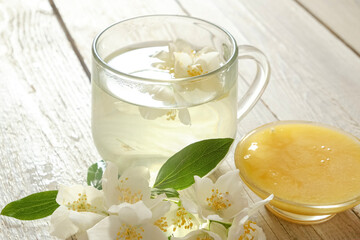 A glass cup of fragrant jasmine tea paired with a bowl of golden honey and fresh jasmine flowers, set on a rustic wooden table. Perfect for wellness, relaxation, and food photography. 