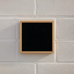 Fototapeta premium Minimalist black square board on a textured white brick wall surface. Minimalist empty message board for custom message on a textured surface.