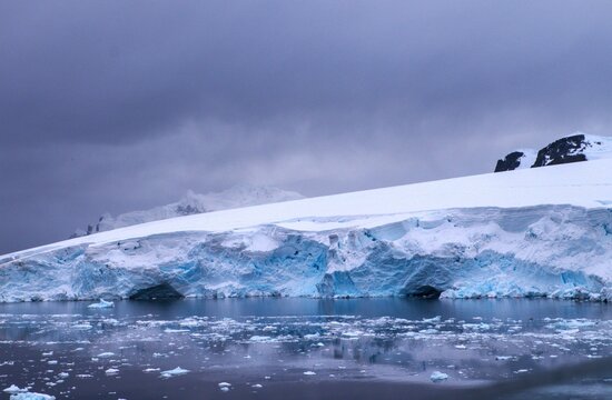 Fascinating Antarctica with a beautiful mountain covered with snow and ice with sunshine on the snowfields in font of the arctic see and some water