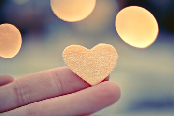 Small pale heart held gently on fingertip, bokeh lights.