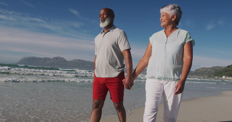 Senior biracial woman and African American man walk on the beach