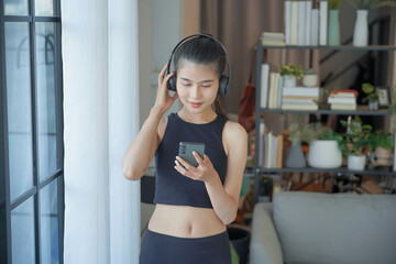 Asian woman in sportswear standing wearing headphone listen to music and holding smartphone