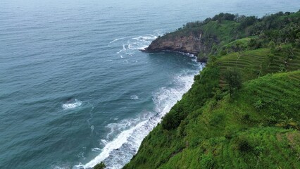 Aerial drone view of coastline with hills and trees, as well as view of coral cliffs and sea with waves from the sea in Menganti Beach Kebumen Central Java Indonesia