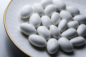 close-up of candy coated white jordan almonds arranged for festive occasion wedding reception gold trim plate background