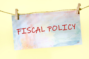 FISCAL POLICY words on a piece of paper fastened with clothespins on a rope on a yellow background