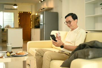 Smiling senior man using a credit card for online payment with mobile phone at home