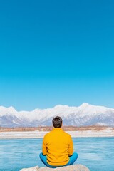 Fototapeta premium Man in Vibrant Yellow Jacket Enjoying Serene Himalayan View by River Under Clear Blue Sky