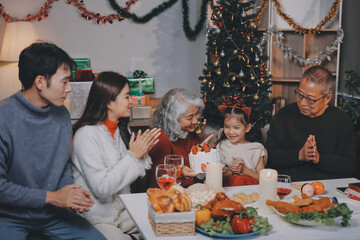 Multi-Generation Family Celebrate Christmas At Home Wearing Santa Hats And Antlers Opening Presents
