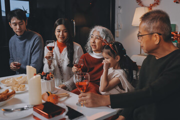 Multi-Generation Family Celebrate Christmas At Home Wearing Santa Hats And Antlers Opening Presents