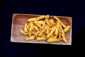 Cheese Puff Snacks on a wooden plate isolated on black background