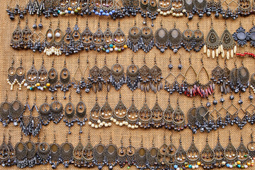 Colorful traditional earrings displayed on a densely packed wall; a variety of intricate designs,...