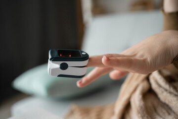 Woman uses pulse oximeter on finger to measure blood oxygen level. Electronic device with monitor shows oxygen saturation and pulse rate, ensuring precise health diagnostics.
