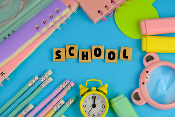 Back to school Concept with note pad, pencils and Paper clips on wooden table. text of SCHOOL on blue background