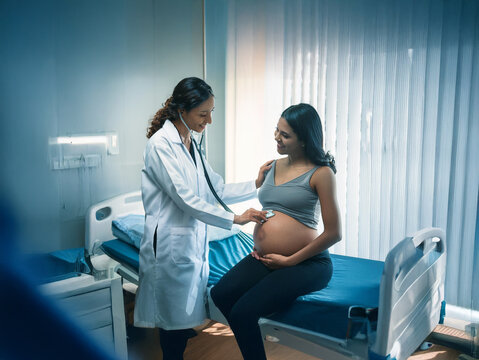 A pregnant woman sits on a hospital bed, smiling as a doctor uses a stethoscope to listen to her baby's heartbeat.  The scene is calm and reassuring.