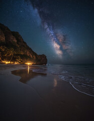 Naklejka premium Starry sky and Milky Way above a dark beach, creating a mysterious and photorealistic nighttime landscape.