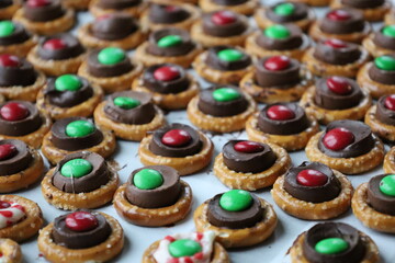 Chocolate pretzels topped with red and green candies on baking sheet