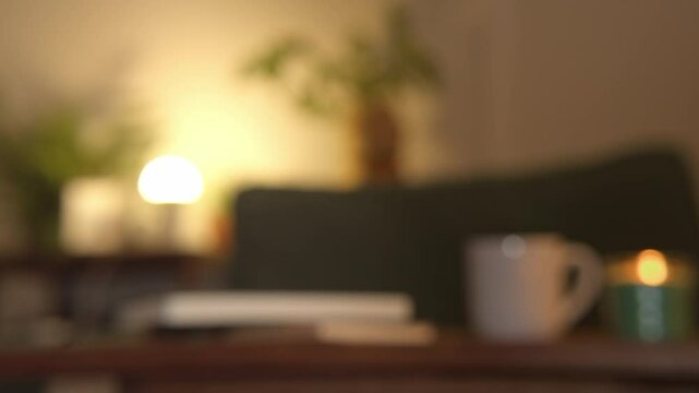 Blurred scene of cozy room in dim light with mug and lit candle. Static