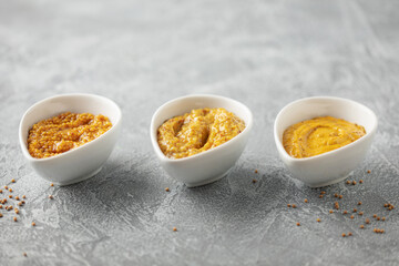 Mustard sauce in a bowl and seeds on a grey background.