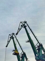 Industrial cranes at a harbor silhouetted against a cloudy sky